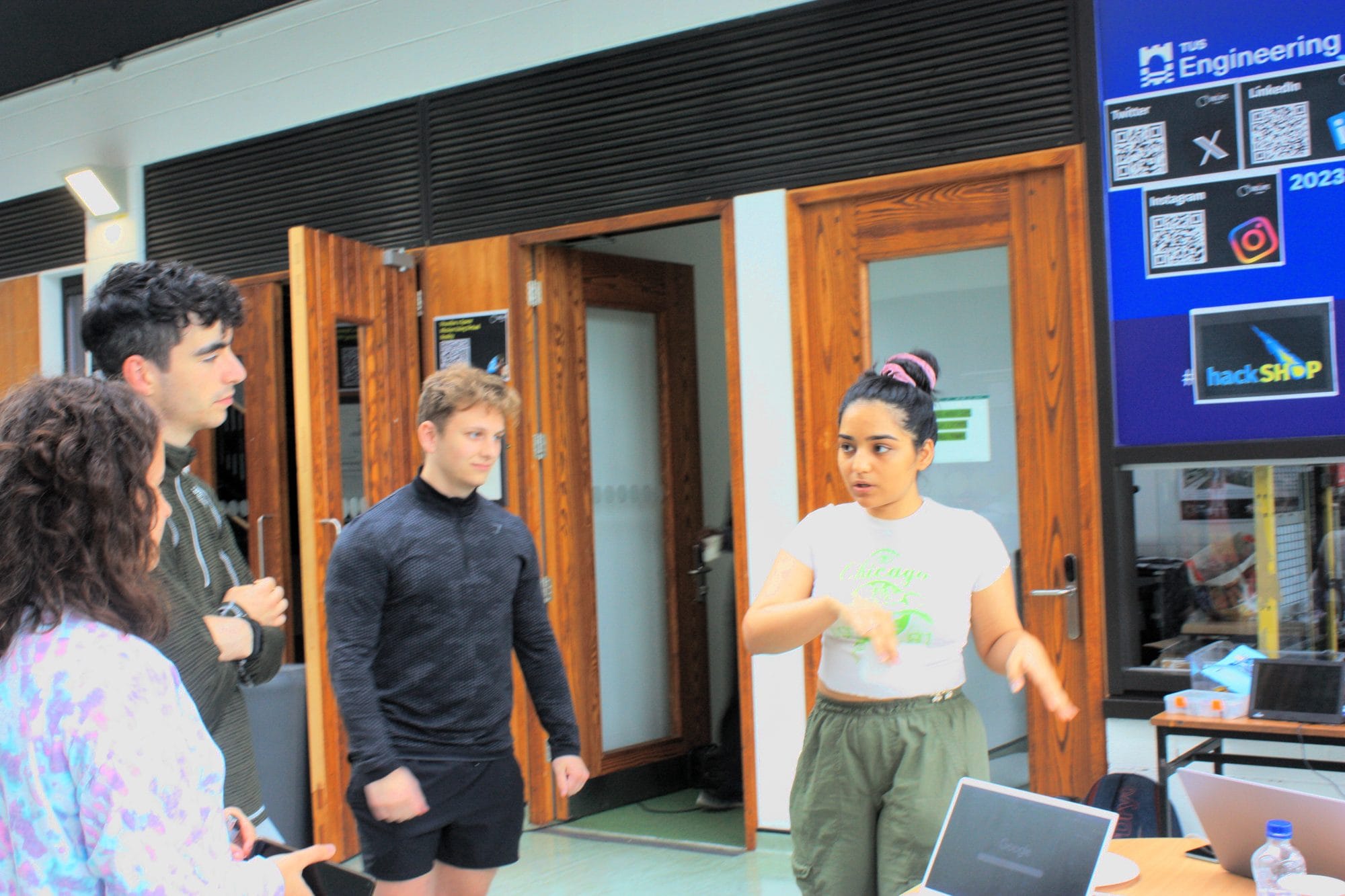 A volunteer talks three participants through something beside the hackSHOP screen at HackAthlone 2023