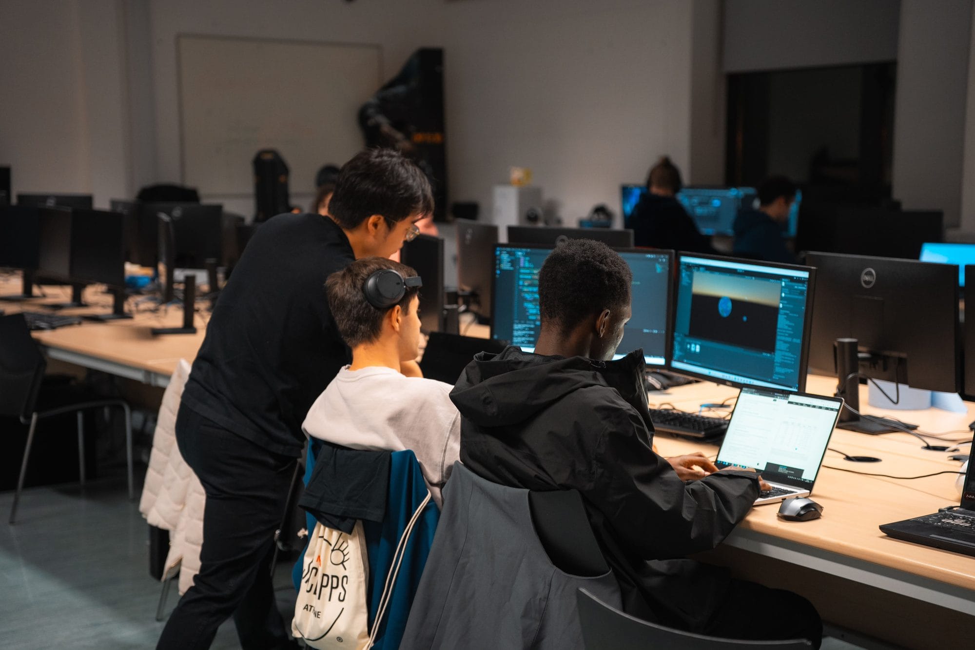 Two participants coding in a TUS computer lab while a third person leans in to look at their screens, at HackAthlone 2025