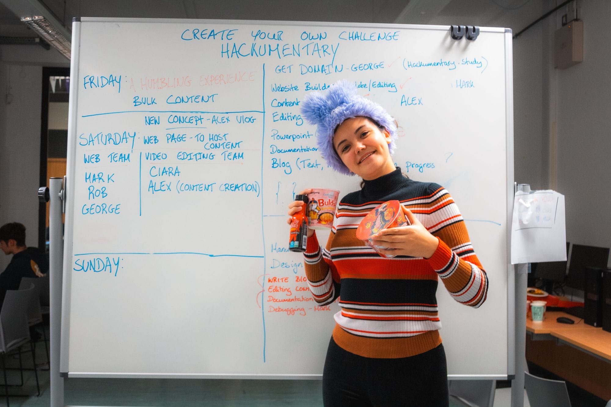 A smiling participant in front of a whiteboard covered in the team’s plan for the weekend